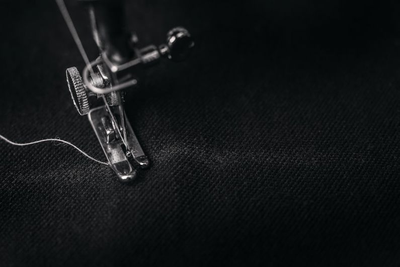 Fabrics - photo of gray sewing machine foot lock with thread on black cloth